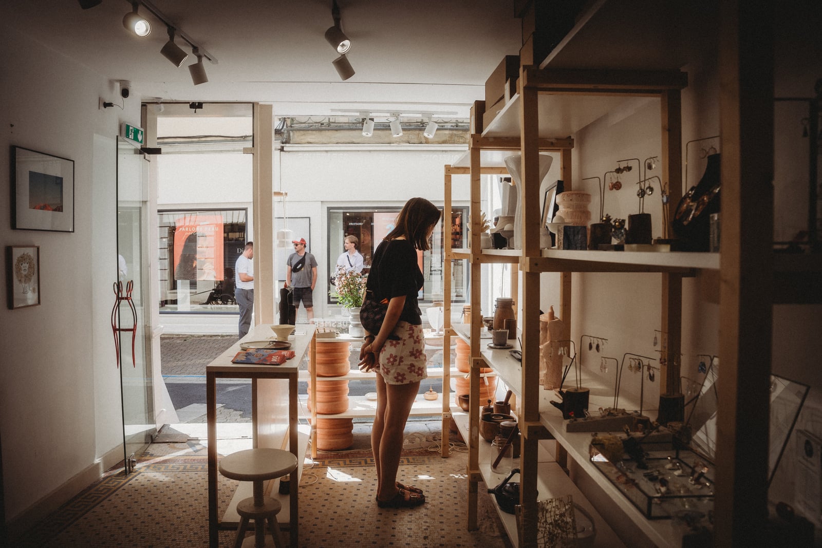 Intérieur d'une boutique : une visiteuse regarde des étagères en bois présentant boucles d'oreilles, colliers et objets artisanaux