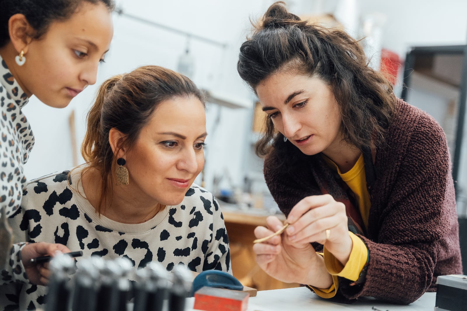 Trois personnes penchées sur un établi pendant un atelier, l'une montrant une fine bande de métal doré